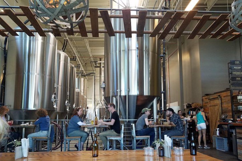 A restaurant with stainless steel tanks, wooden tables, and people dining. 4