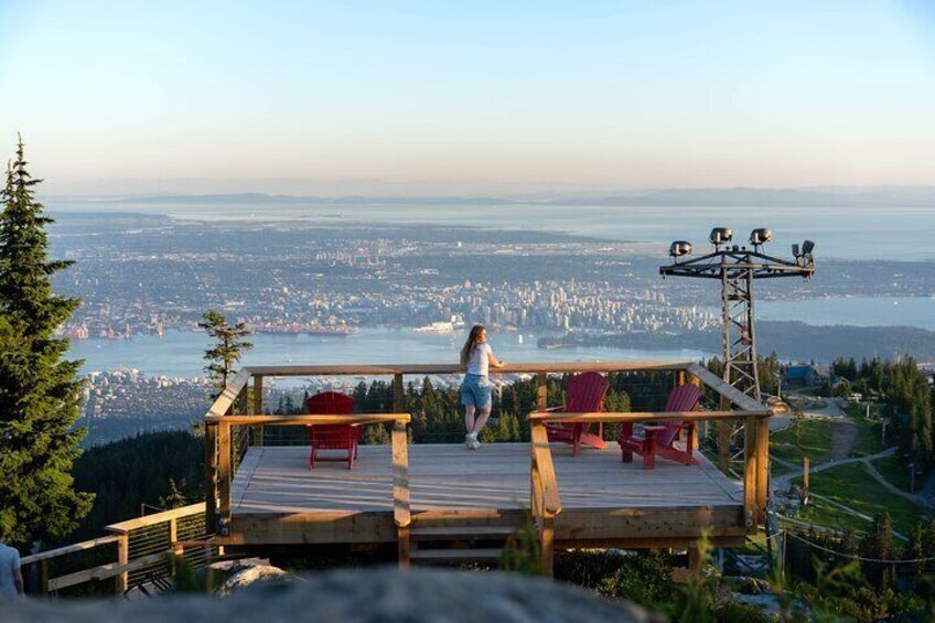 A wooden deck with red chairs overlooking a cityscape and a body of water. 4