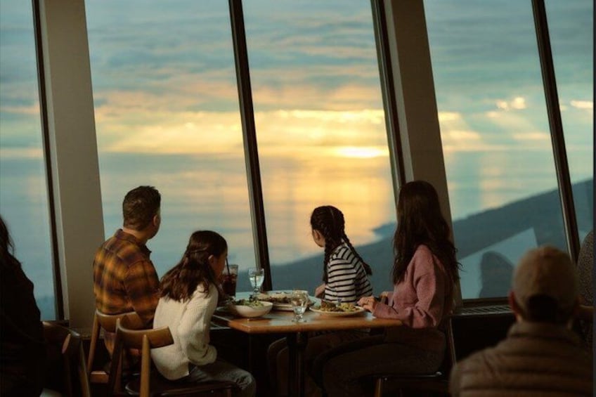 Un grupo de personas cenando en una mesa con vista al atardecer. 2