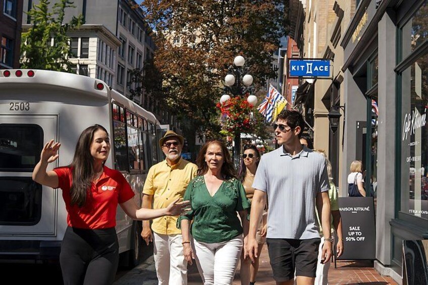 A group of people walking on a city street with a bus and storefronts. 4