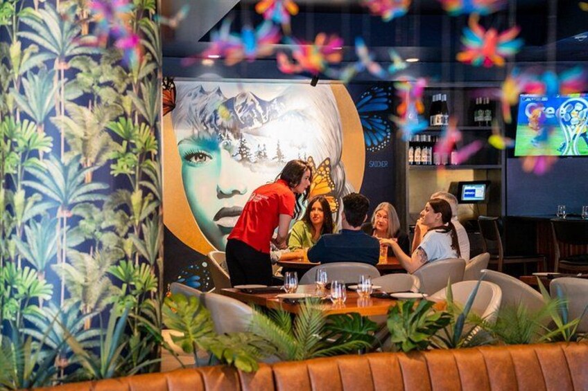 A group of people seated around a table in a restaurant with a mural of a woman's face on the wall. 3