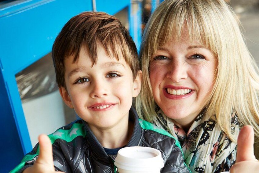 Two children with thumbs up, one holding a cup, in front of a blue structure. 3