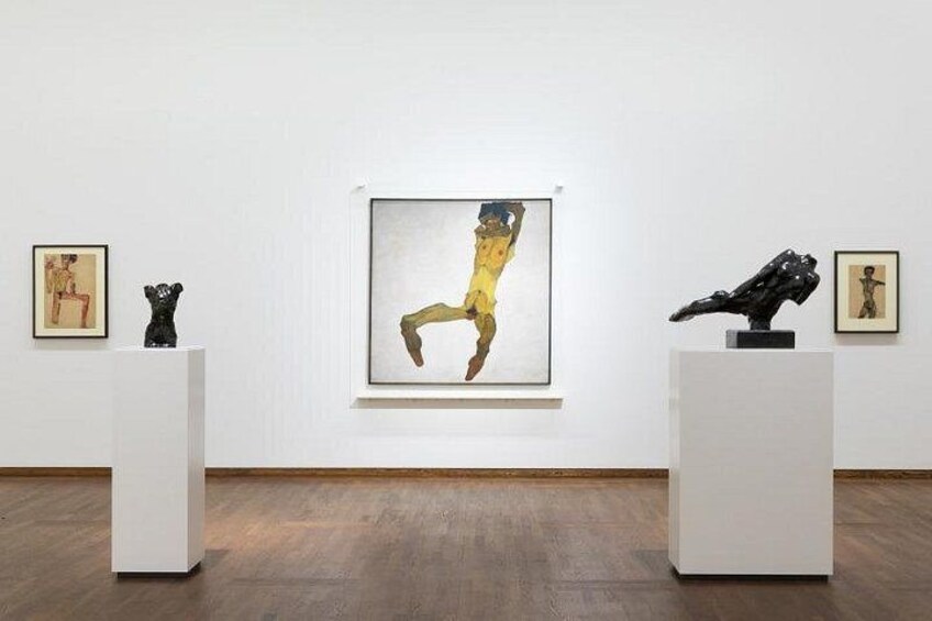 Una galería de arte con un cuadro grande de una figura en amarillo y negro, dos esculturas en pedestales y obras de arte enmarcadas en las paredes. 4