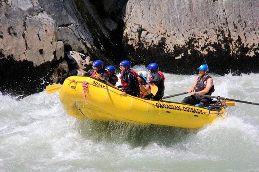 A yellow inflatable raft with people wearing helmets and life jackets navigating through white water rapids. 2
