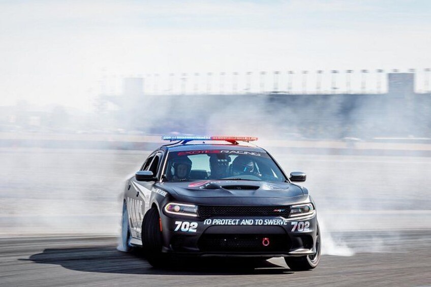 A police car with the number 702 performing a burnout on a track. 4
