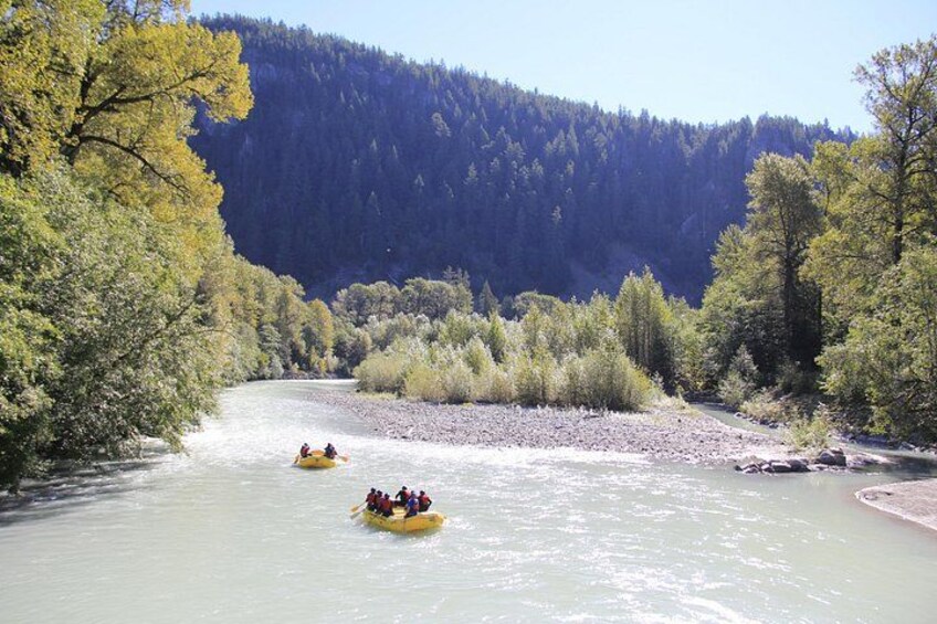 A river with two yellow boats, surrounded by trees and a forested hill. 2