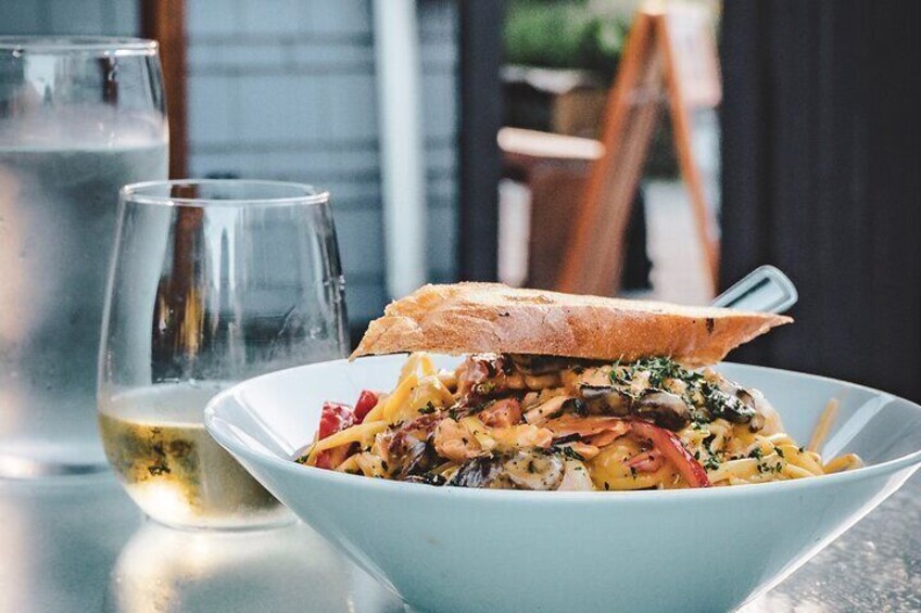 A bowl of pasta with a piece of bread on top, a glass of white wine, and a glass of water on a table. 5