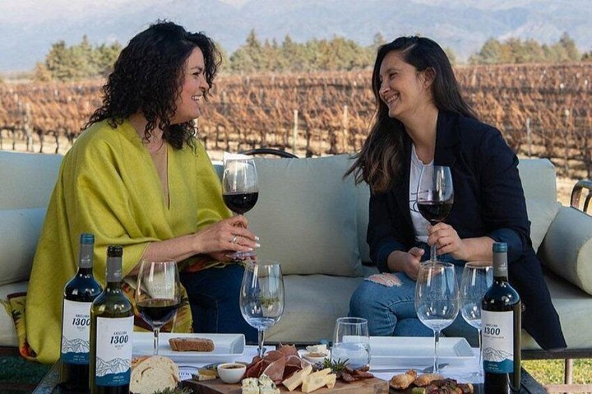 Two people sitting on a couch outdoors with wine glasses and bottles on a table. 5