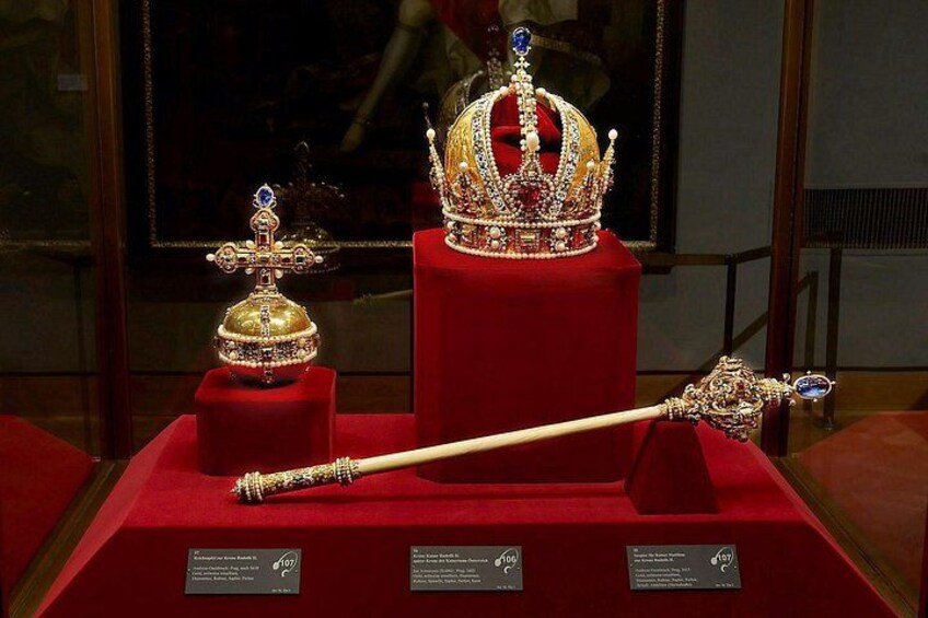 A display of a golden crown, a scepter, and a jeweled orb on a red velvet stand. 5
