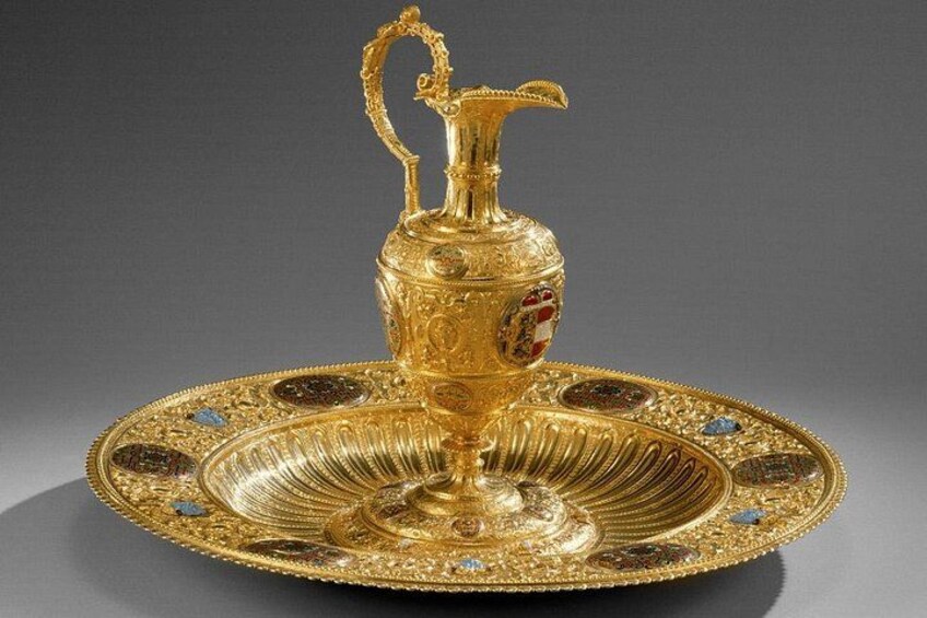 A golden ornate pitcher with a handle, placed on a decorative plate with intricate designs and gemstones. 4