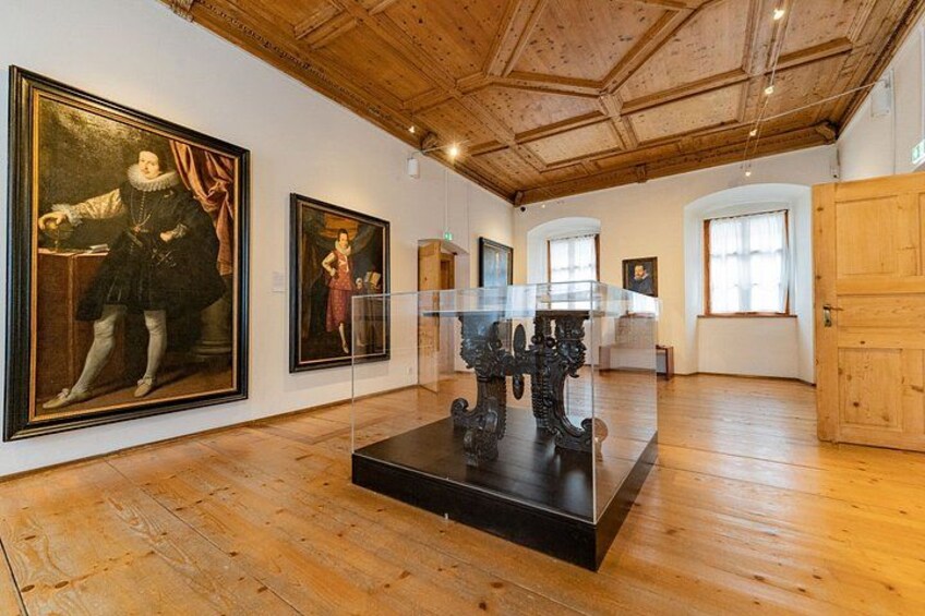 An art gallery with wooden floors, paintings, and a glass display case. 2