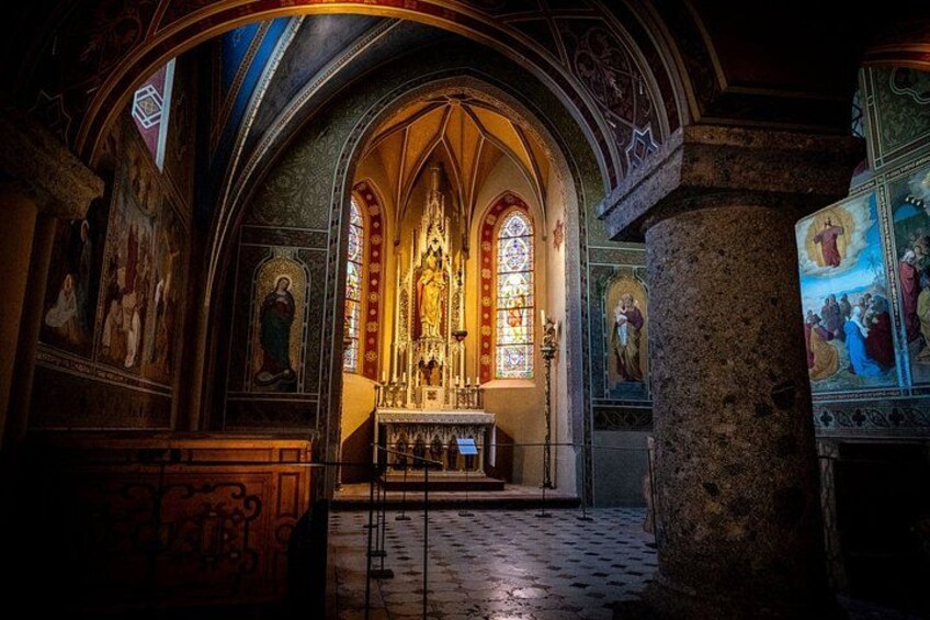 An interior of a church with a high altar, stained glass windows, and religious paintings. 3