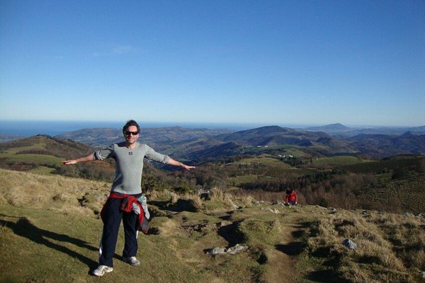 A person standing on a grassy hill with arms outstretched, overlooking a valley with rolling hills and a clear sky. 5