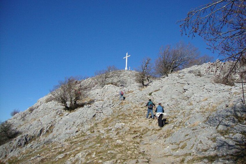 A rocky hill with a cross, people hiking, and sparse vegetation. 4
