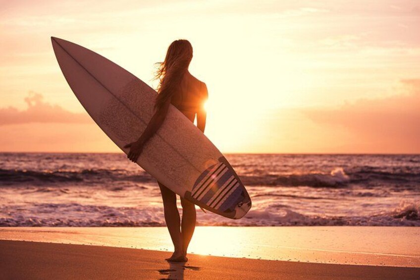 Una persona sostiene una tabla de surf en la playa al atardecer. 2