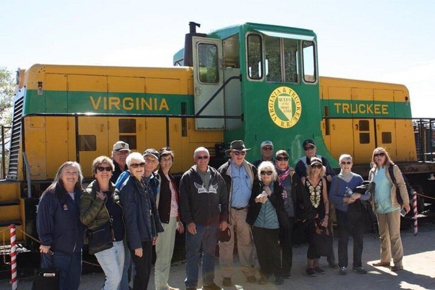 A group of people standing in front of a yellow and green train with 'VIRGINIA' and 'TRUCKEE' written on it. 3