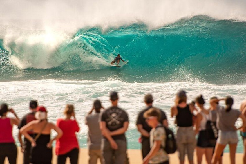 Un surfeur chevauchant une grosse vague, tandis qu'une foule observe depuis la plage. 3