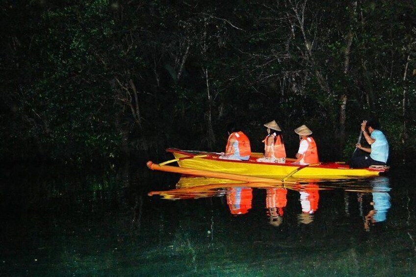 A yellow canoe with three people wearing hats and orange life jackets on a calm river surrounded by dense trees. 4