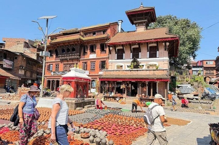 Un mercato con diversi prodotti esposti a terra, un edificio con tetto rosso e persone che fanno acquisti. 4