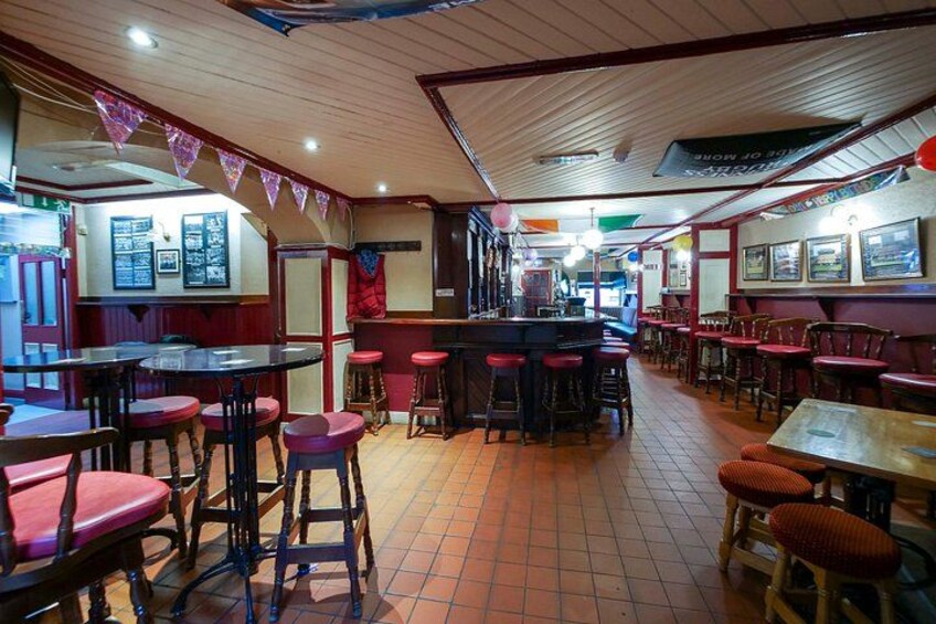 Ein Restaurantinneres mit Holztischen und roten Hocker, einer Bar und Fliesenboden. 4