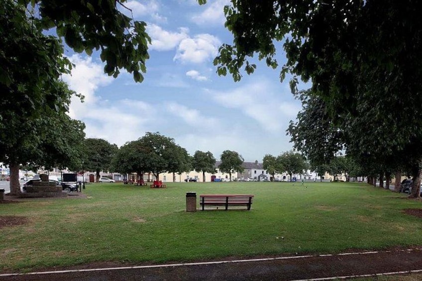 Ein Park mit einer Rasenfläche, einer Bank, Bäumen und einer Reihe von Gebäuden im Hintergrund. 5