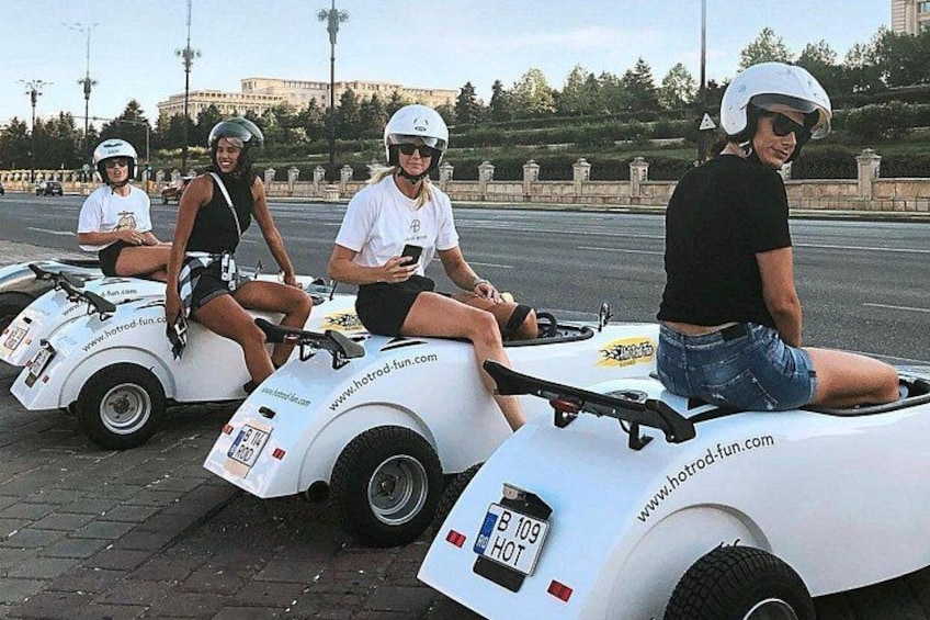 Cuatro personas en vehículos blancos pequeños con ruedas, con un sitio web indicado, sobre una superficie pavimentada. 3