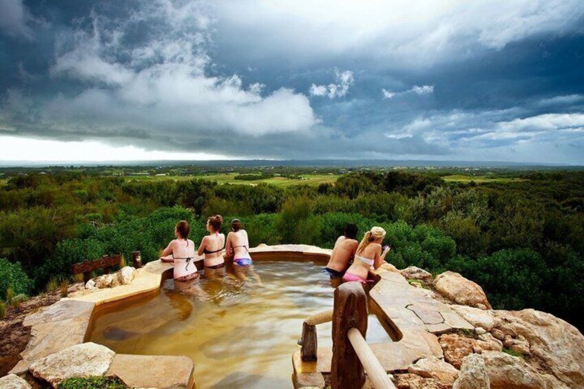 A group of people in a natural hot spring surrounded by greenery and a cloudy sky. 1
