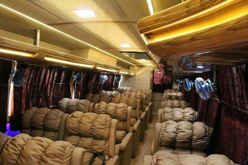 A train interior with rows of seats, overhead luggage racks, and fans. 1