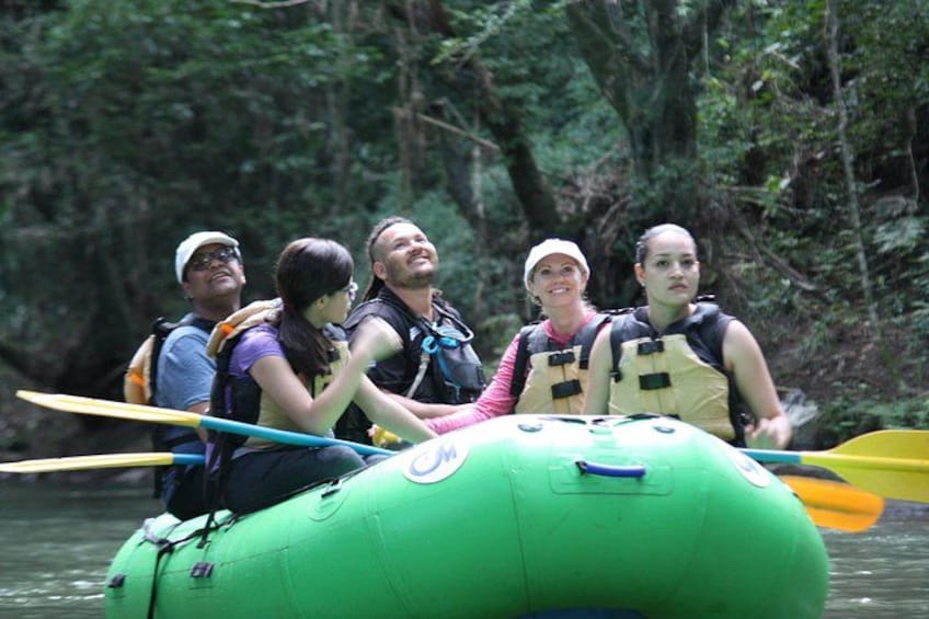 A group of people in a green inflatable raft on a river surrounded by dense forest. 2