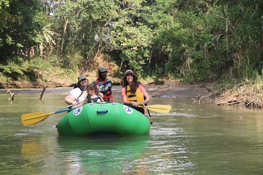 A green raft with paddles, surrounded by a river and dense greenery. 1