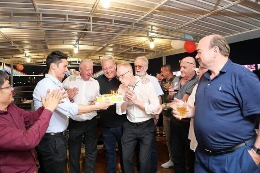Un grupo de hombres celebrando con un pastel y bebidas en un espacio exterior techado. 2