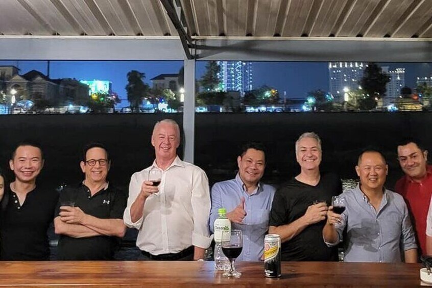 Un grupo de personas de pie en una barra, con bebidas, una botella de refresco y una copa de vino sobre la mesa. 3
