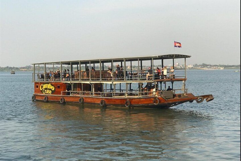 Un barco de madera con toldo, identificado como 'Cambodia Cruise', navegando sobre aguas tranquilas. 1
