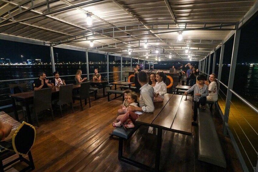 Un espacio cubierto para comer al aire libre con mesas y sillas de madera, con vistas a un cuerpo de agua por la noche. 5