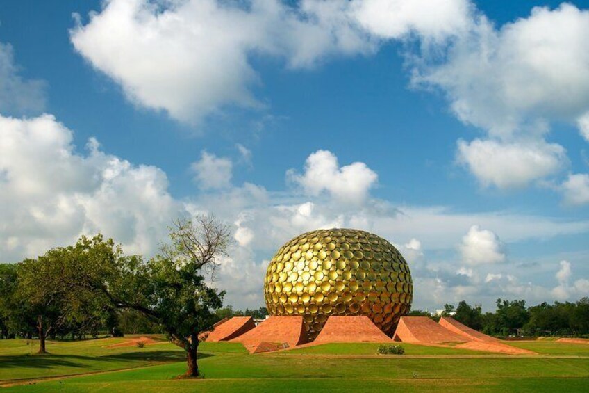 A large golden geodesic dome structure in a park with green grass and trees. 2