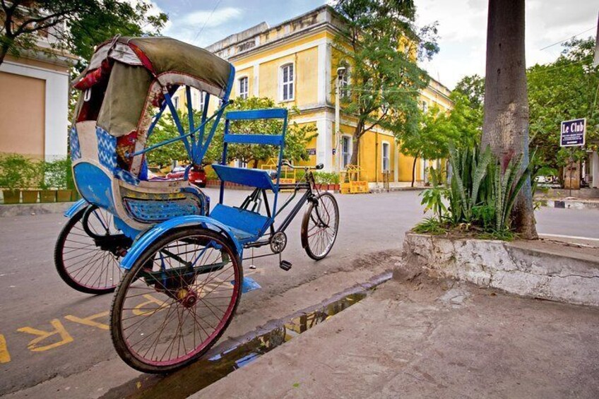 A blue rickshaw parked on a street with a yellow building in the background. 4