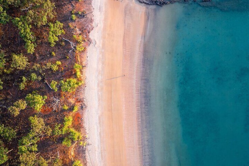An aerial view of a beach with clear turquoise water and a sandy shore. 1