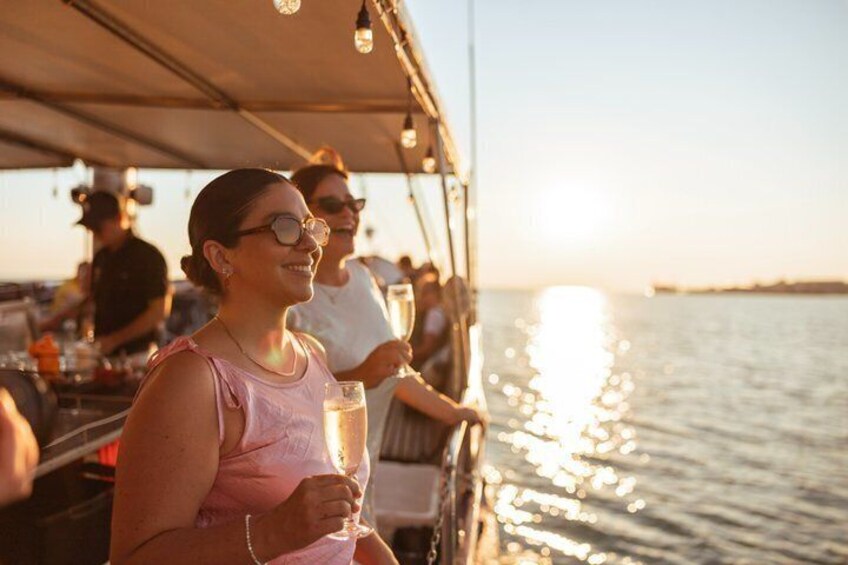 Una persona sostiene un vaso con una bebida en un barco, con un atardecer de fondo. 1