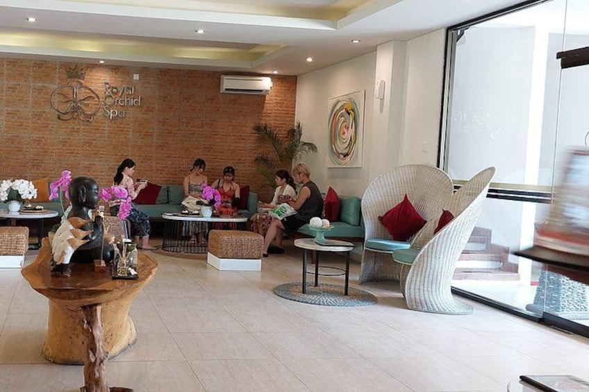Vestíbulo de spa con paredes de ladrillo, un mostrador de recepción y varias zonas de estar con gente. 2