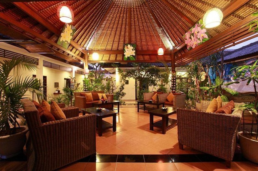 Un salón interior con muebles de mimbre, plantas en macetas y suelo de baldosas. 1