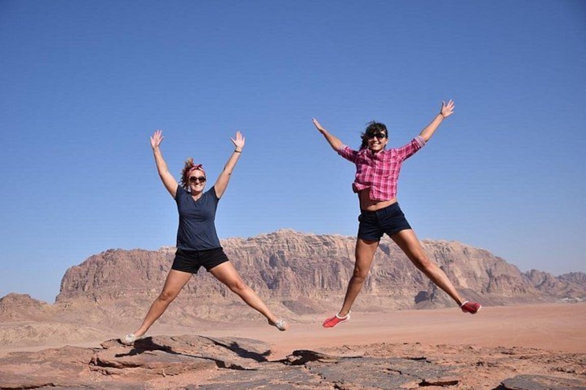 Two people jumping in a desert landscape with rocky terrain and mountains in the background. 2