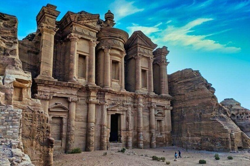 A large sandstone structure with columns and a doorway, surrounded by rocky terrain. 1