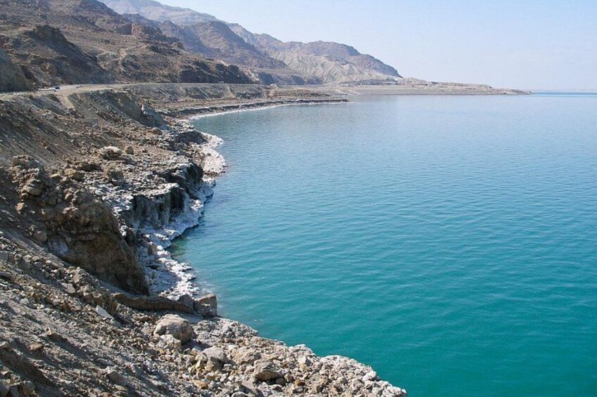 A coastal landscape with a rocky shoreline, calm turquoise waters, and distant mountains. 2