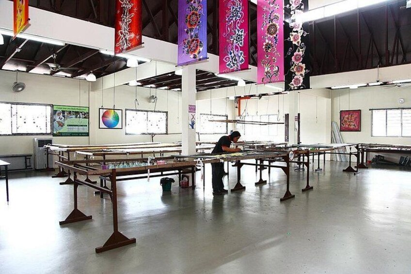 A spacious room with tables and chairs, banners hanging from the ceiling, and a person working at one of the tables. 2