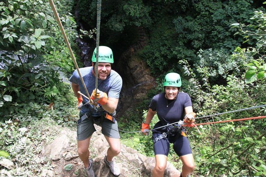 Two people rappelling down a rocky cliff with ropes, surrounded by dense foliage. 4
