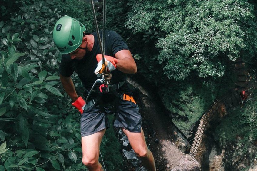 A person rappelling down a rocky cliff surrounded by dense foliage. 2