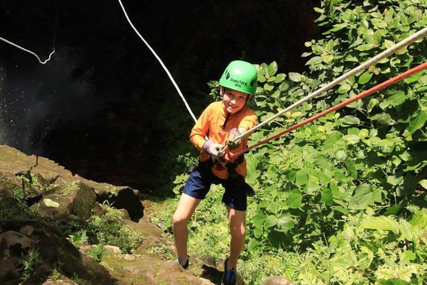 A person rappelling down a rocky cliff with ropes, surrounded by greenery. 3