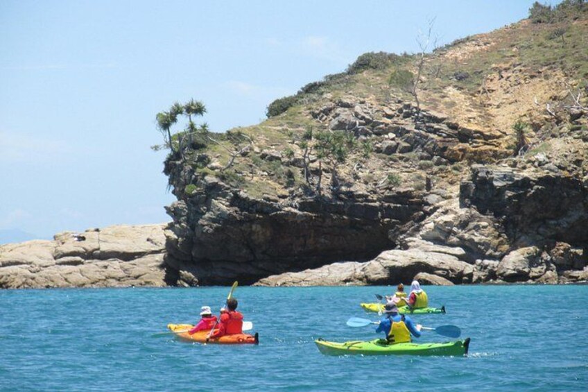 Deux personnes pratiquent le kayak sur une mer calme, avec des falaises rocheuses en arrière-plan. 5