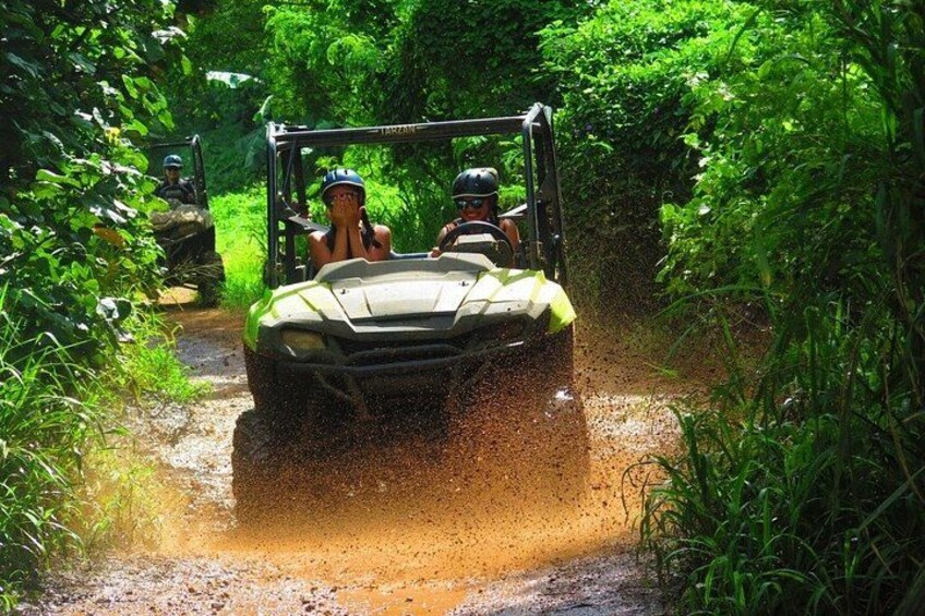 A vehicle driving through a muddy path surrounded by dense greenery. 2