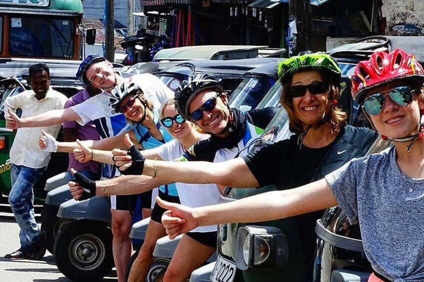 Un gruppo di persone su una bicicletta tandem, con una strada e auto parcheggiate sullo sfondo. 3
